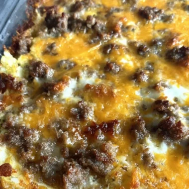 Sausage Hashbrown Breakfast Casserole baked in a dish, topped with cheese and herbs