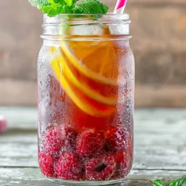 A refreshing glass of Earl Grey Raspberry Iced Tea with berries and lemon slices.
