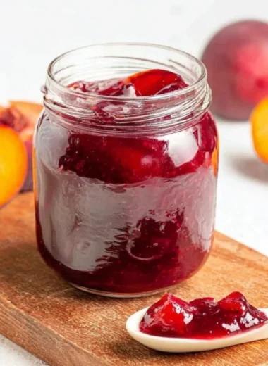 Homemade plum jam in a jar with fresh plums on a wooden table