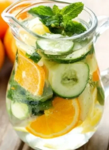 A refreshing glass of orange cucumber and mint water garnished with fresh mint leaves.