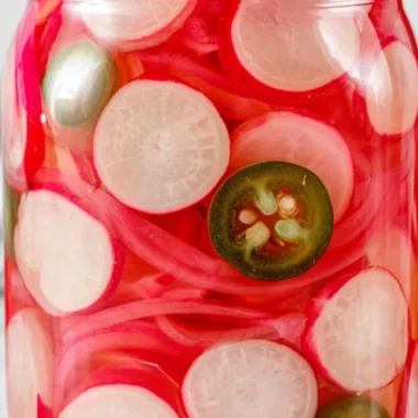 Quick pickled radishes in a glass jar with spices