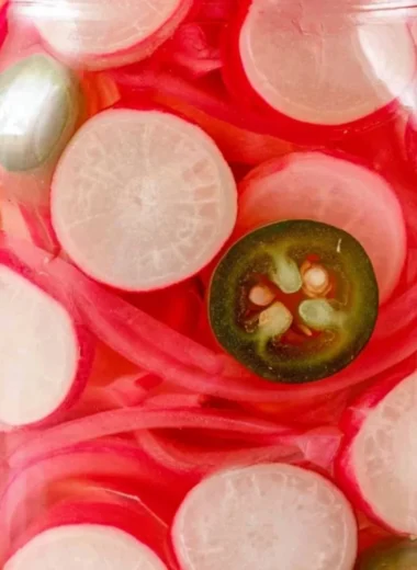 Quick pickled radishes in a glass jar with spices