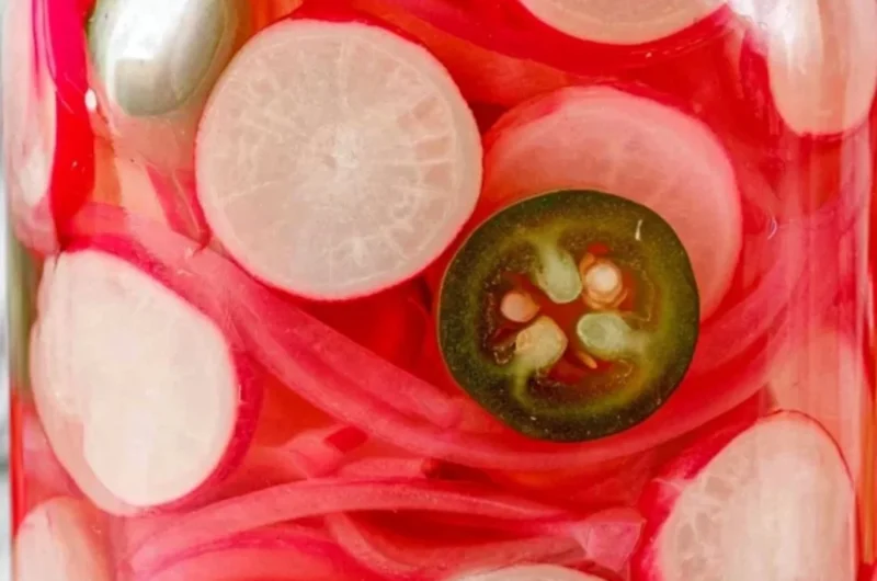 Quick pickled radishes in a glass jar with spices