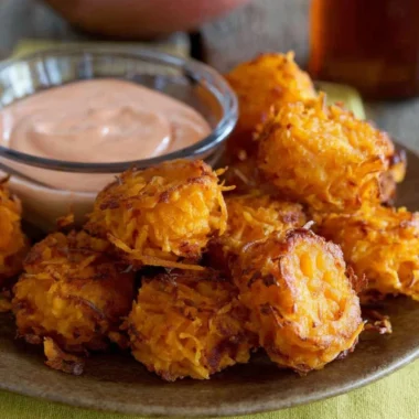 Bowl of crispy sweet potato tots served with dipping sauce.