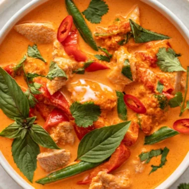 A bowl of cozy Thai red curry with chicken, vibrant spices, and fresh herbs.