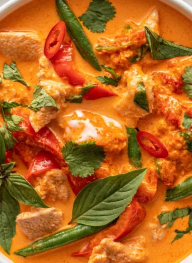 A bowl of cozy Thai red curry with chicken, vibrant spices, and fresh herbs.