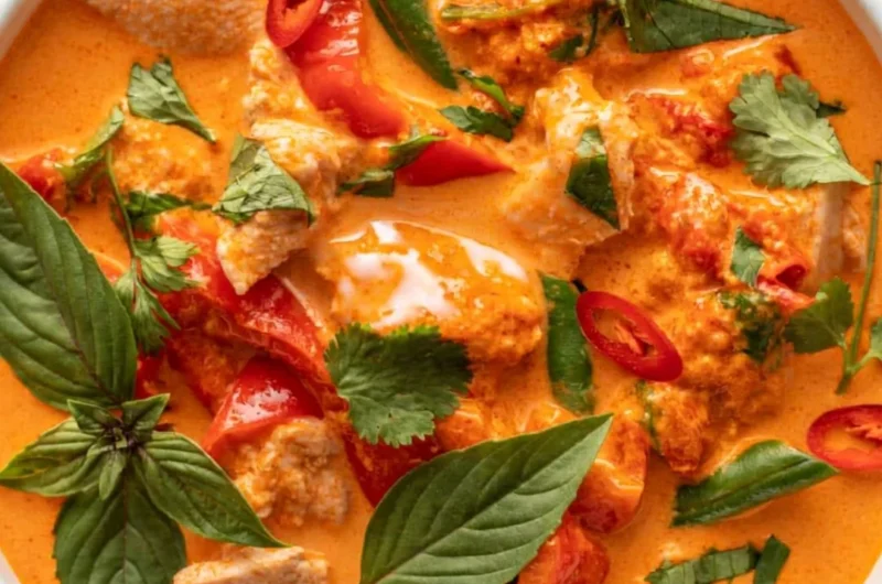 A bowl of cozy Thai red curry with chicken, vibrant spices, and fresh herbs.