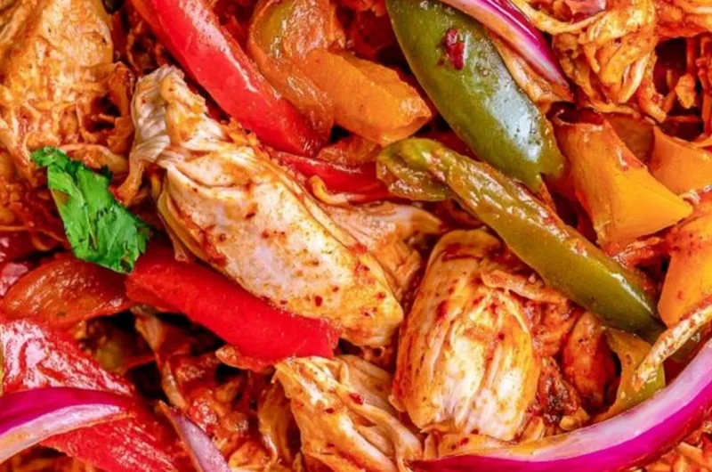 Bowl of crockpot chicken fajitas with colorful peppers and onions.
